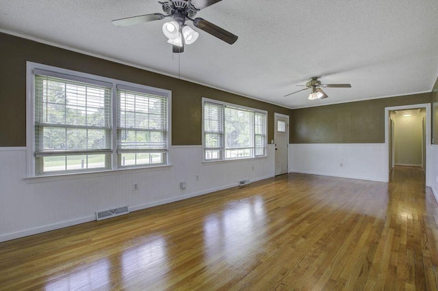 spare room with a textured ceiling, light wood-style flooring, wainscoting, and visible vents