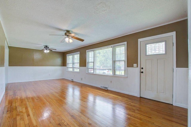 foyer with a wainscoted wall, a textured ceiling, visible vents, and light wood-style floors