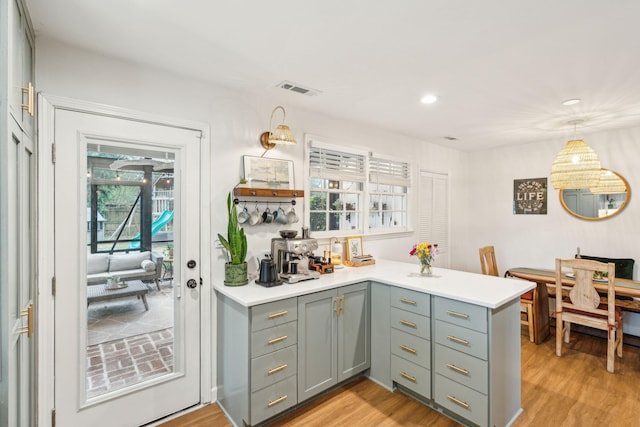 kitchen with a peninsula, visible vents, light countertops, light wood finished floors, and decorative light fixtures