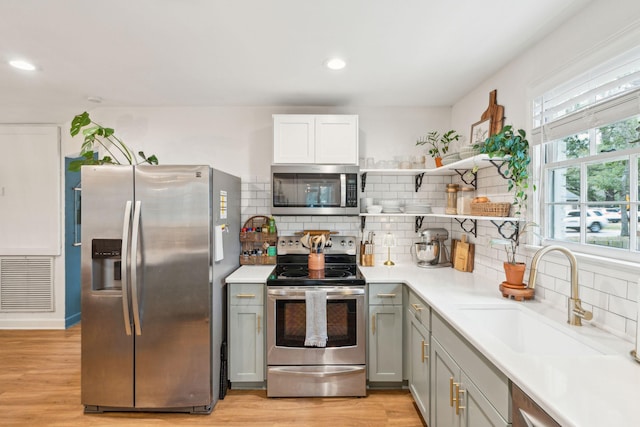 kitchen with gray cabinetry, a sink, light countertops, appliances with stainless steel finishes, and open shelves