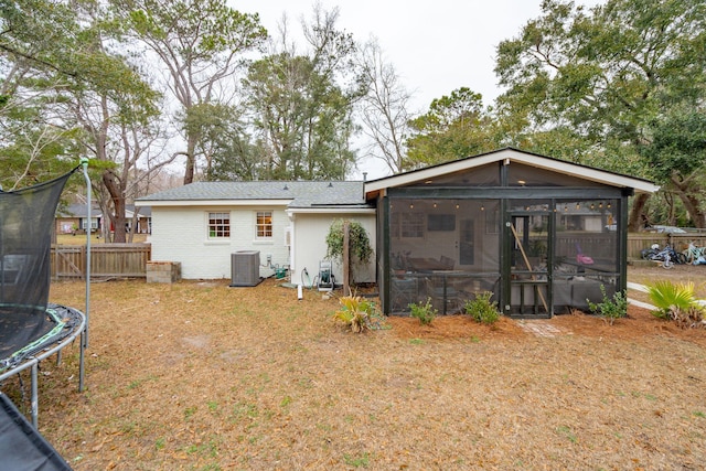 rear view of property with central air condition unit, brick siding, fence, a sunroom, and a trampoline