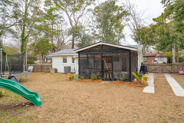 back of property with a trampoline, a playground, central air condition unit, a sunroom, and a fenced backyard