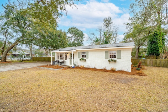 ranch-style house with a porch, a front yard, brick siding, and fence