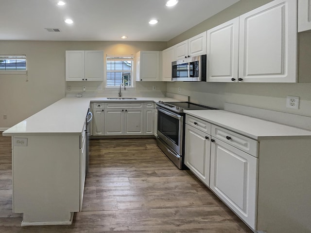 kitchen with sink, appliances with stainless steel finishes, hardwood / wood-style floors, white cabinets, and kitchen peninsula