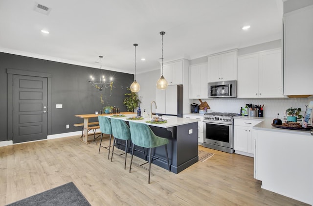 kitchen with white cabinetry, pendant lighting, stainless steel appliances, and an island with sink