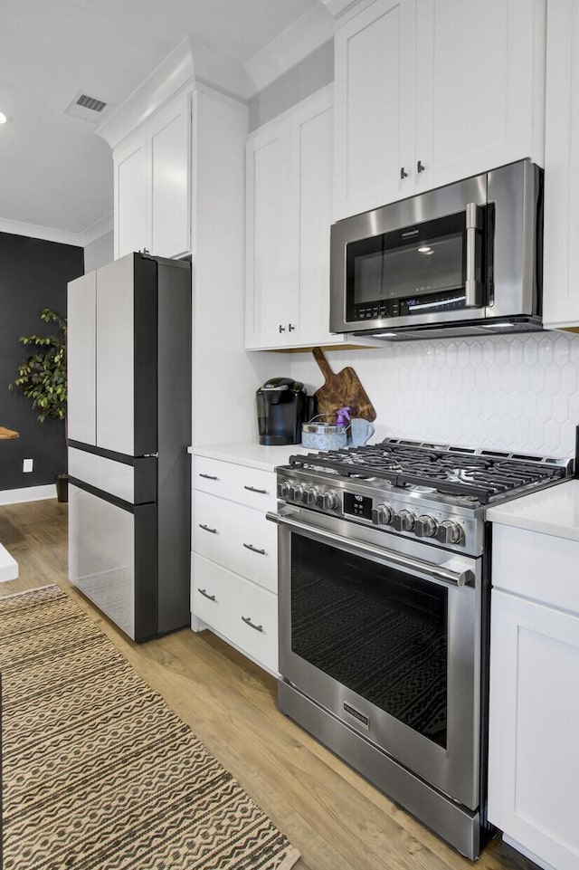 kitchen featuring crown molding, appliances with stainless steel finishes, white cabinetry, backsplash, and light wood-type flooring