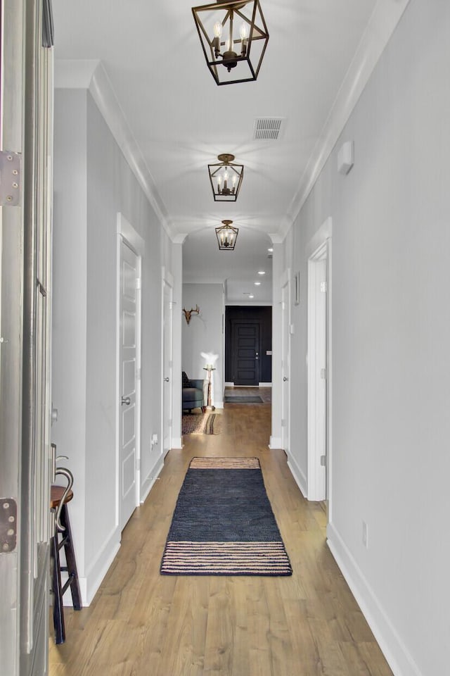 hallway featuring hardwood / wood-style floors, ornamental molding, and a chandelier