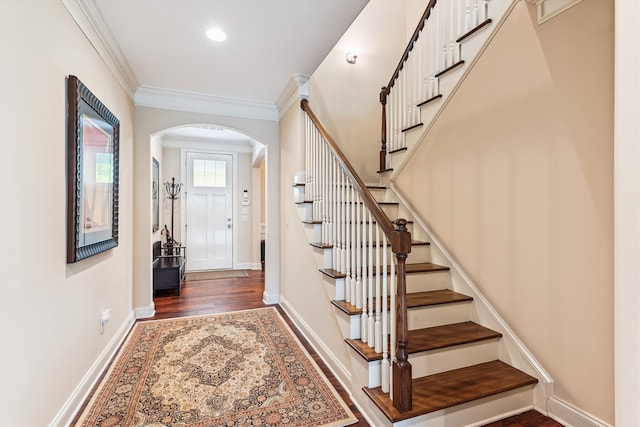 foyer featuring arched walkways, wood finished floors, stairs, ornamental molding, and baseboards