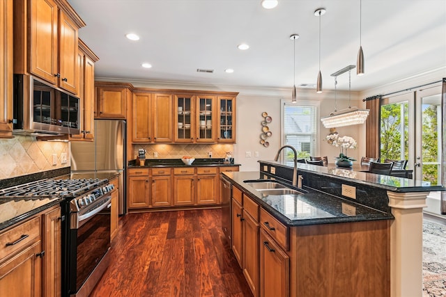 kitchen featuring appliances with stainless steel finishes, a sink, brown cabinets, dark wood-type flooring, and ornamental molding