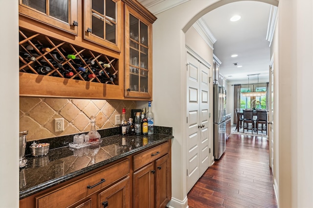 indoor dry bar with arched walkways, ornamental molding, dark wood finished floors, backsplash, and freestanding refrigerator