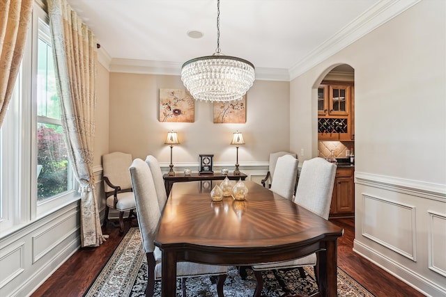 dining room with dark wood-style flooring, crown molding, arched walkways, a wainscoted wall, and a chandelier