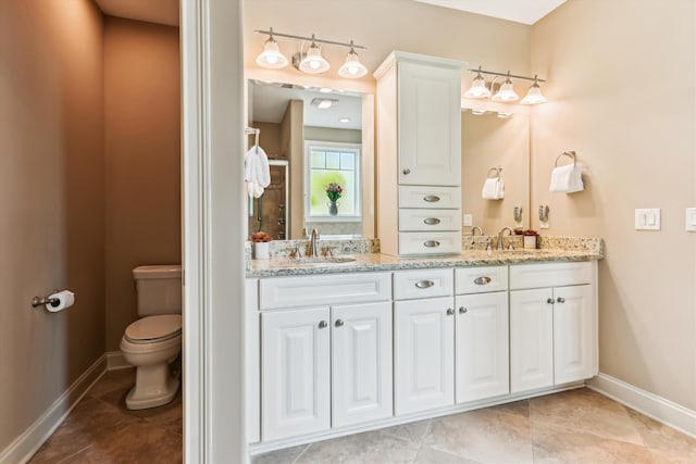 bathroom featuring toilet, baseboards, double vanity, and tile patterned floors
