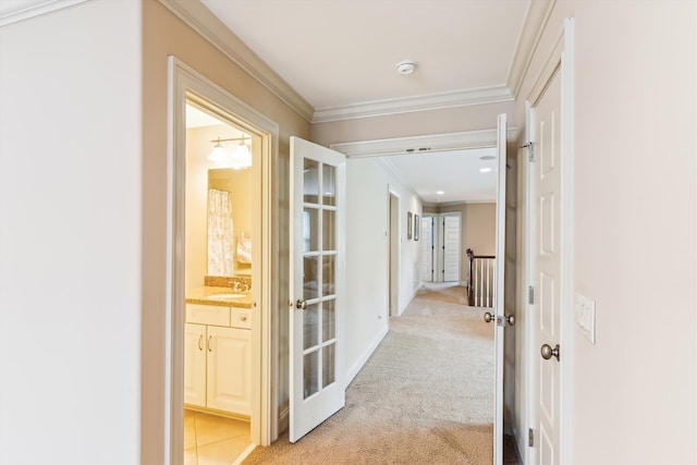 hallway with a sink, ornamental molding, light carpet, and baseboards