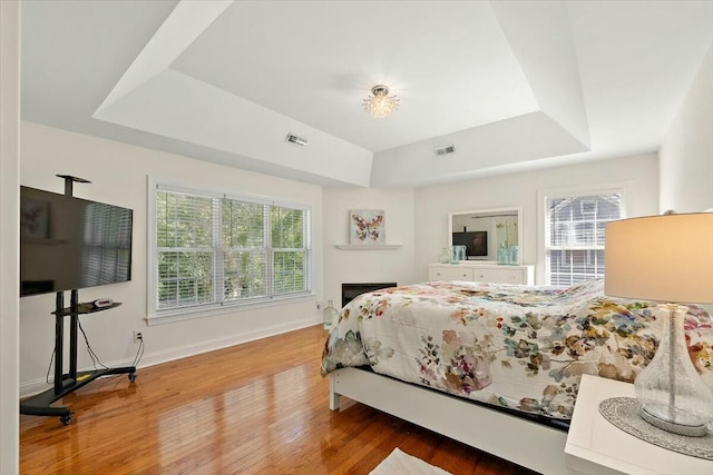 bedroom featuring hardwood / wood-style flooring, multiple windows, and a tray ceiling