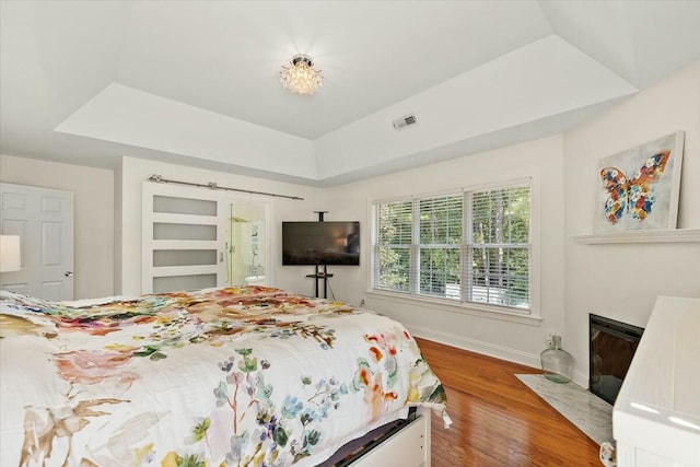 bedroom featuring hardwood / wood-style floors, a tray ceiling, and a barn door