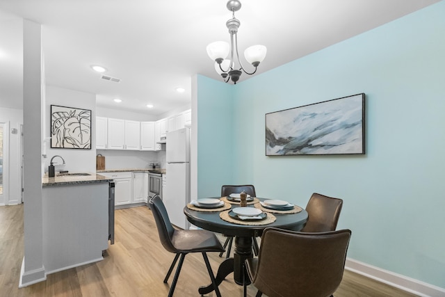 dining room with sink, a chandelier, and light hardwood / wood-style flooring