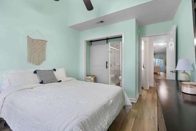 bedroom featuring ceiling fan, a barn door, ensuite bathroom, hardwood / wood-style floors, and a closet