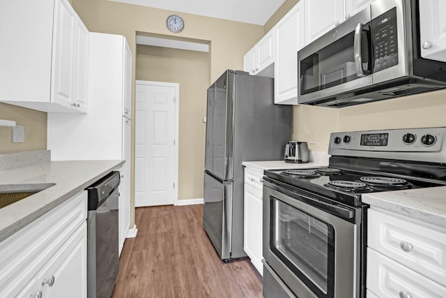 kitchen with appliances with stainless steel finishes, light hardwood / wood-style flooring, white cabinetry, and light stone countertops