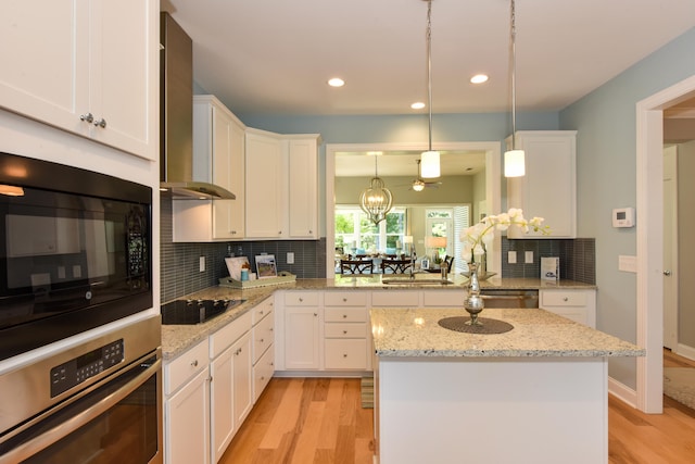 kitchen featuring wall chimney exhaust hood, black appliances, white cabinetry, and hanging light fixtures