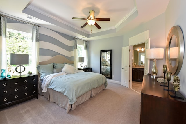 bedroom featuring a raised ceiling, ceiling fan, ensuite bathroom, ornamental molding, and light carpet