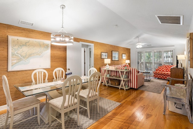 dining area featuring wood-type flooring, ceiling fan with notable chandelier, wooden walls, and lofted ceiling