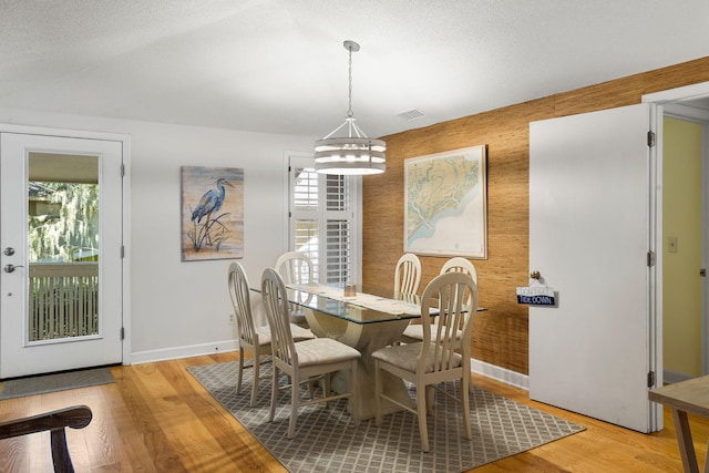 dining area with an inviting chandelier, a textured ceiling, wood walls, and light hardwood / wood-style floors