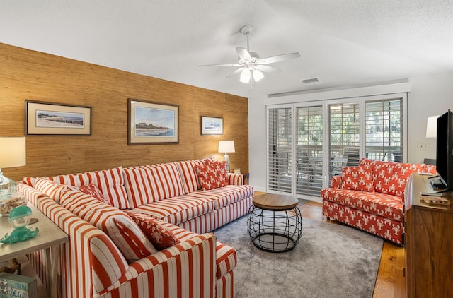 living room with ceiling fan, wood walls, hardwood / wood-style floors, and a textured ceiling