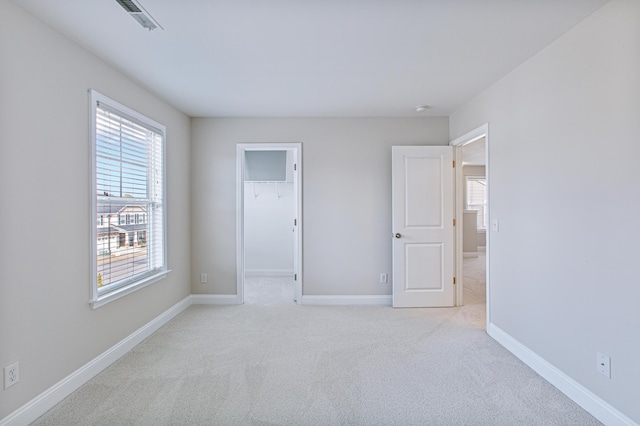 unfurnished bedroom featuring baseboards, a spacious closet, multiple windows, and light colored carpet