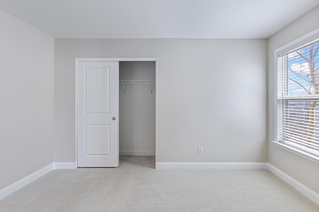 unfurnished bedroom with a closet, light carpet, and baseboards