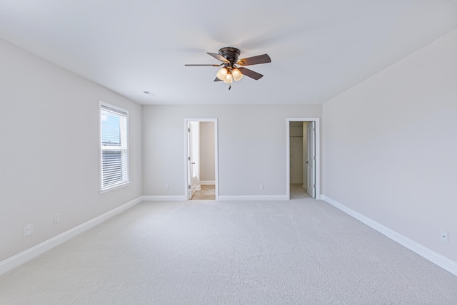 unfurnished bedroom featuring ceiling fan, light carpet, visible vents, baseboards, and a walk in closet