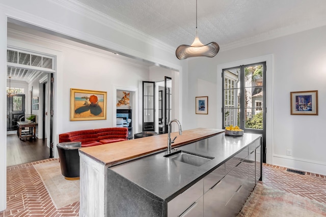 kitchen with sink, hanging light fixtures, an island with sink, a textured ceiling, and ornamental molding