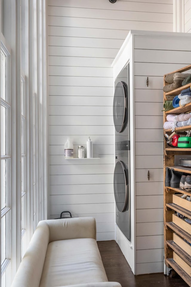 laundry room featuring wooden walls, dark hardwood / wood-style flooring, and stacked washing maching and dryer