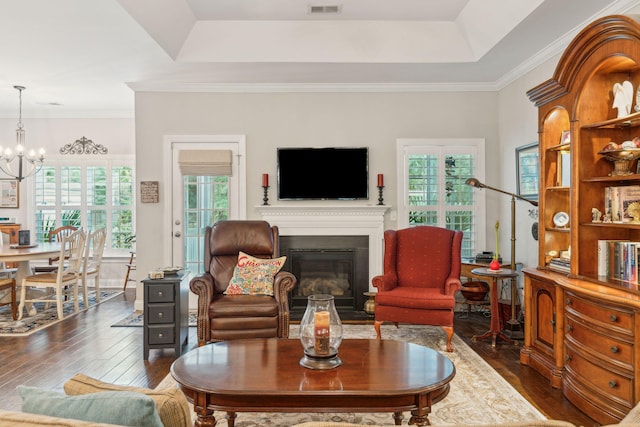 living room featuring a tray ceiling, a notable chandelier, dark hardwood / wood-style floors, and ornamental molding