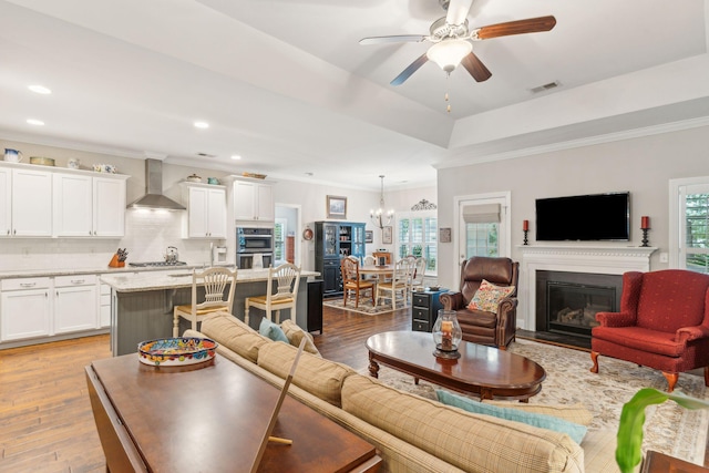 living room with ceiling fan with notable chandelier, light wood-type flooring, and ornamental molding