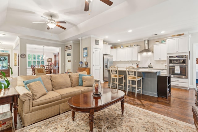 living room featuring a tray ceiling, crown molding, dark wood-type flooring, and ceiling fan with notable chandelier