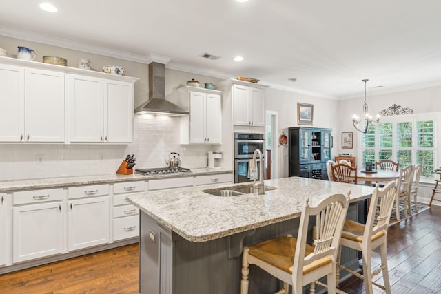 kitchen featuring sink, wall chimney range hood, a kitchen island with sink, and dark wood-type flooring