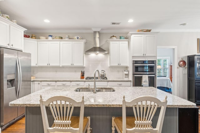 kitchen featuring white cabinetry, wall chimney range hood, stainless steel appliances, and a kitchen island with sink