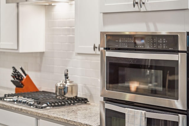 kitchen with stainless steel appliances, decorative backsplash, white cabinets, and light stone counters