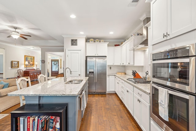 kitchen with white cabinets, ornamental molding, light stone counters, appliances with stainless steel finishes, and dark hardwood / wood-style flooring