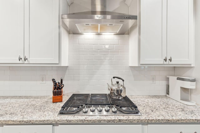 kitchen featuring tasteful backsplash, white cabinetry, stainless steel gas stovetop, and wall chimney exhaust hood