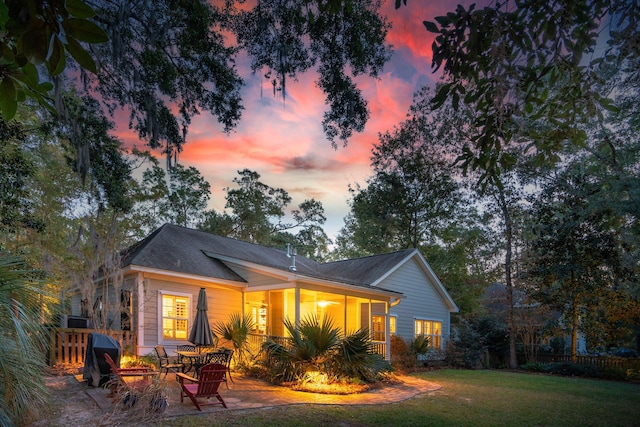 back house at dusk with a lawn and a patio area