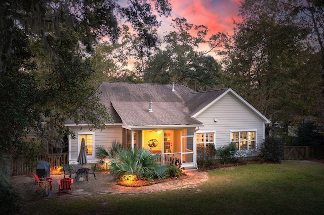 back house at dusk with a lawn, a patio area, and a sunroom