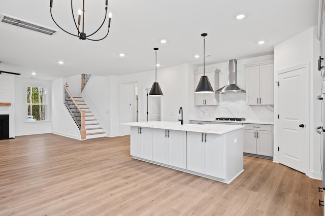 kitchen with decorative light fixtures, white cabinets, a center island with sink, and wall chimney exhaust hood