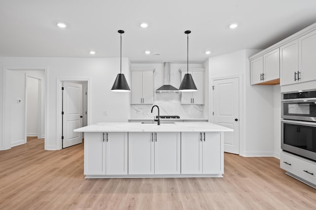 kitchen featuring white cabinetry, decorative light fixtures, wall chimney range hood, and a kitchen island with sink