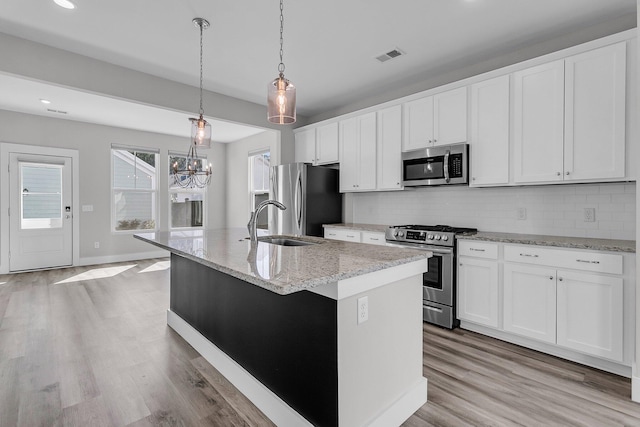 kitchen with hanging light fixtures, a center island with sink, stainless steel appliances, light stone countertops, and white cabinets