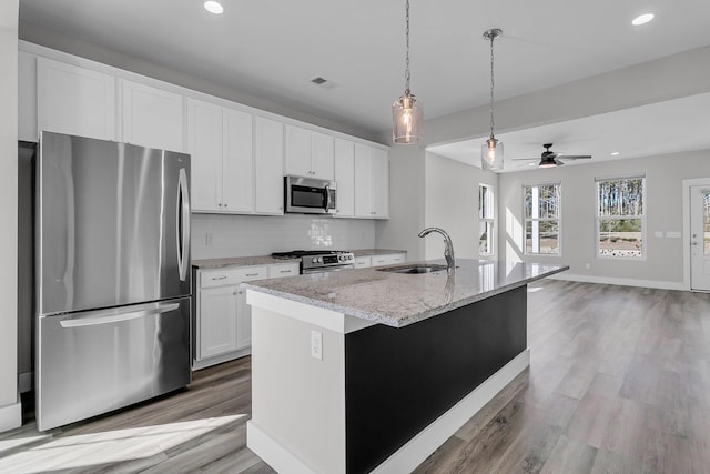 kitchen with appliances with stainless steel finishes, an island with sink, sink, white cabinets, and light stone countertops