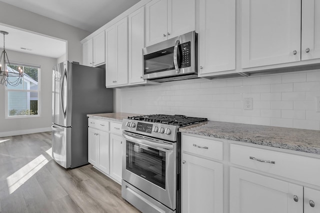 kitchen featuring light wood finished floors, stainless steel appliances, tasteful backsplash, white cabinetry, and light stone countertops