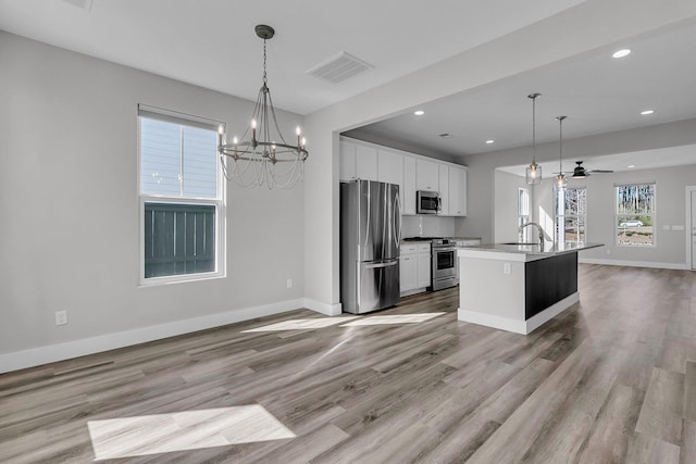 kitchen with sink, appliances with stainless steel finishes, an island with sink, white cabinets, and decorative light fixtures