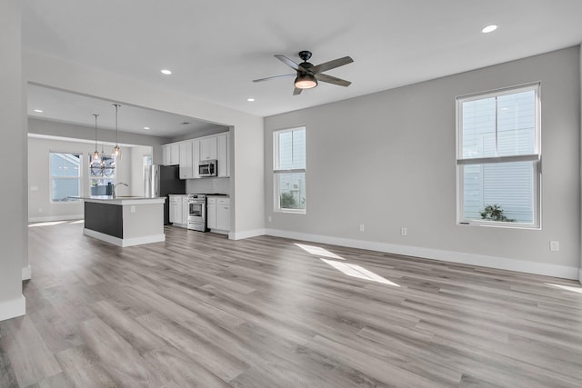 unfurnished living room featuring plenty of natural light, sink, ceiling fan with notable chandelier, and light wood-type flooring