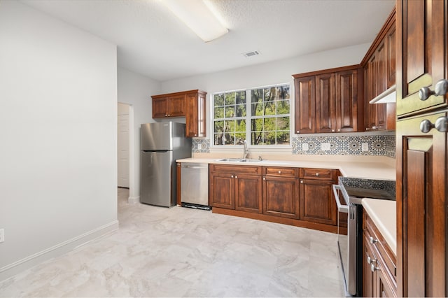 kitchen featuring a textured ceiling, backsplash, stainless steel appliances, and sink